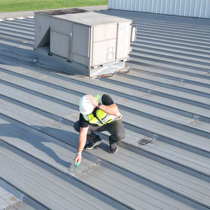 roofer with lime green safety vest inspecting the integrity of metal roof