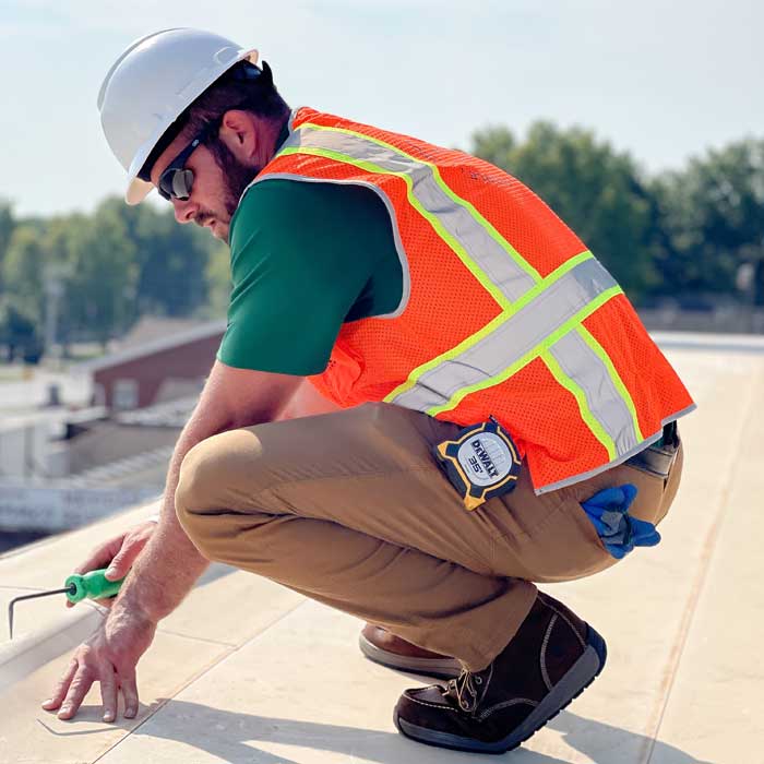 roofer crouching as he inspects a commercial roof integrity